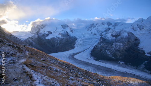 Sunrise over mountain chain above Monte Rosa massif. First rays of the sun over mountains. Male hiker on a trail to the new Monte Rosa hut along the Border Glacier Grenz Gletscher. Vacation in Zermatt photo