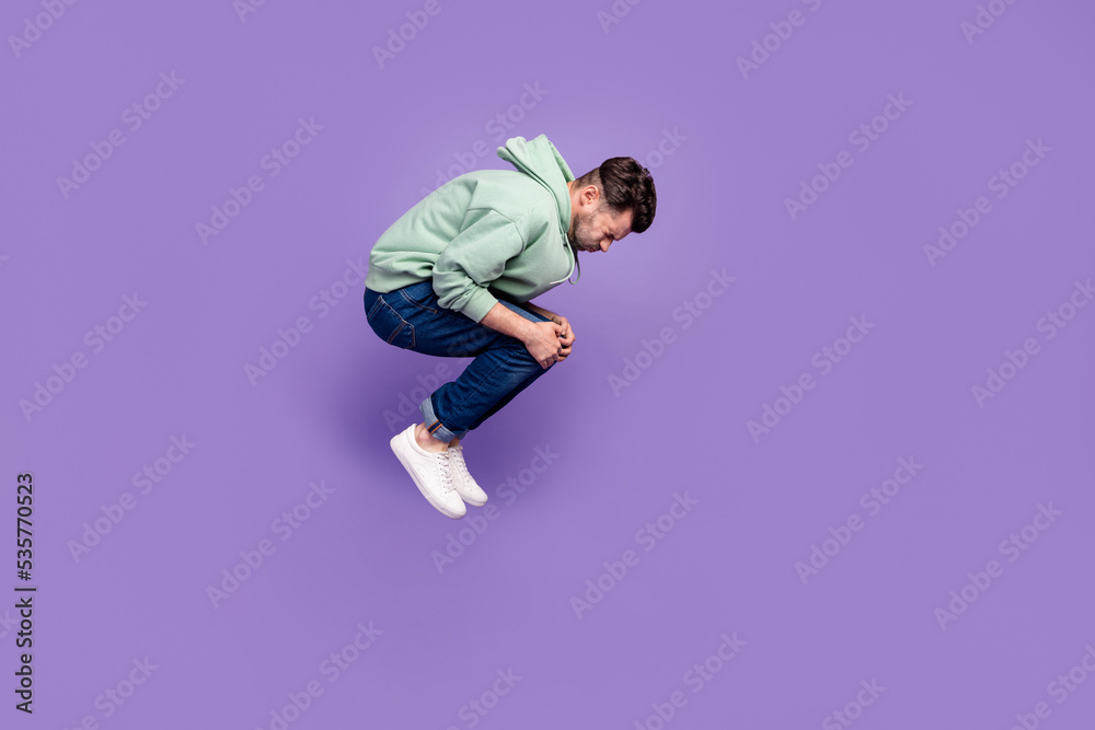 Full size profile photo of falling young man hands hold knees isolated on violet color background Full size profile photo of falling young man hands hold knees isolated on violet color background