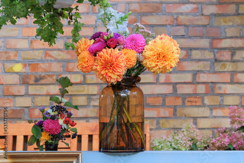 Roses, asters, dahilia in glass vase in the garden on the background of a brick wall. Sunny day. Floristic design. photo