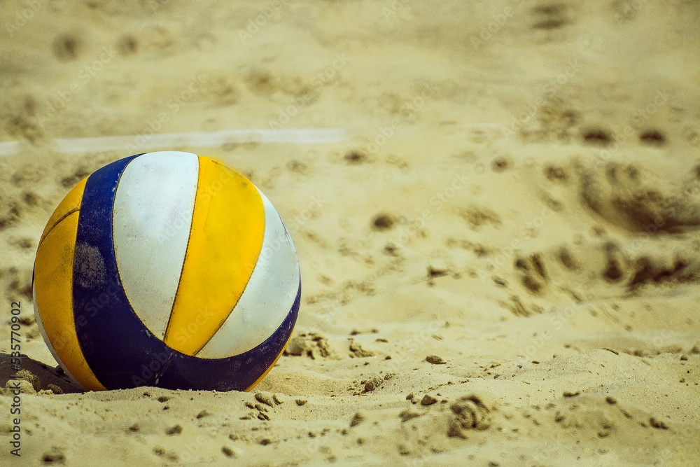 A blue volleyball with yellow and white stripes lies on the sand	
