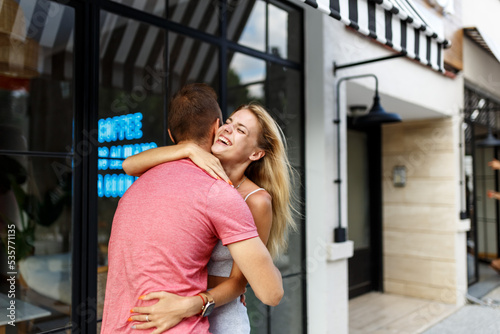 Farewell concept. Delighted happy smiling blonde woman says goodbye or hi to boyfriend, gives warm hug, pose together against cafe place. Truthful feelings