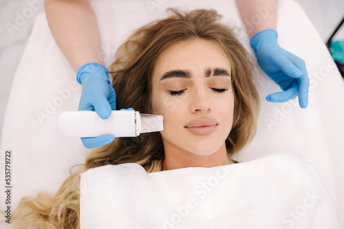 Close up of female face with soft skin. Woman at cosmetology clinic taking a beauty procedure for skin. Beautician using peeling device, ultrasonic clining. Gorgeous woman