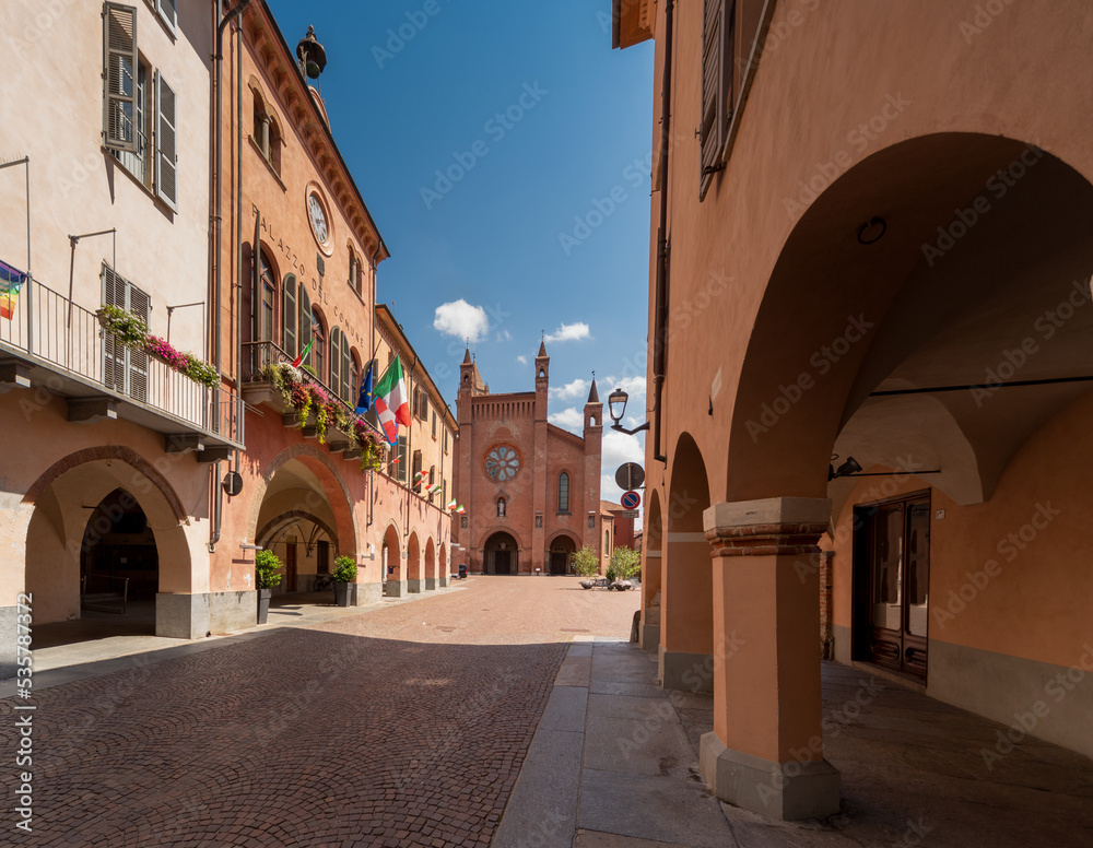 Alba, Langhe, Piedmont, Italy - August 16, 2022: via Cavour with medieval arcades and the Town Hall with flowered balconies, in the background Cathedral of San Lorenzo in Piazza Duomo