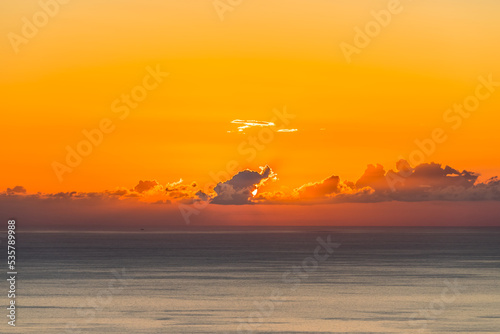 Seascape with sunset and the sun behind the dark clouds on a blue sea background