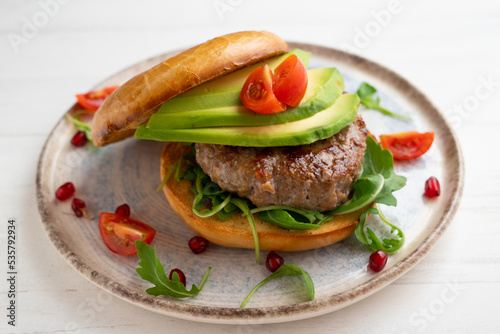 Toasted bagel with premium beef burger, arugula, and avocado slices.