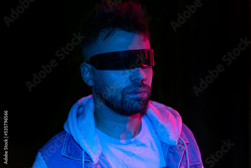 Neon light studio close-up portrait of serious man model with mustaches and beard in cyberpunk sunglasses  photo