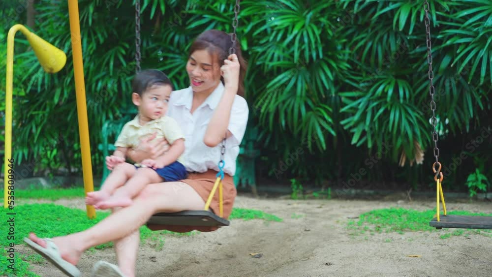 Asian sit on swing and her son on lap with happiness playing together in park or garden with morning light. Asian sit on swing and her son on lap with happiness playing together in park or garden with morning light.