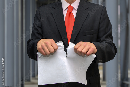 Photography A man in a suit and tie tears up a sheet of paper against the background of metal structures