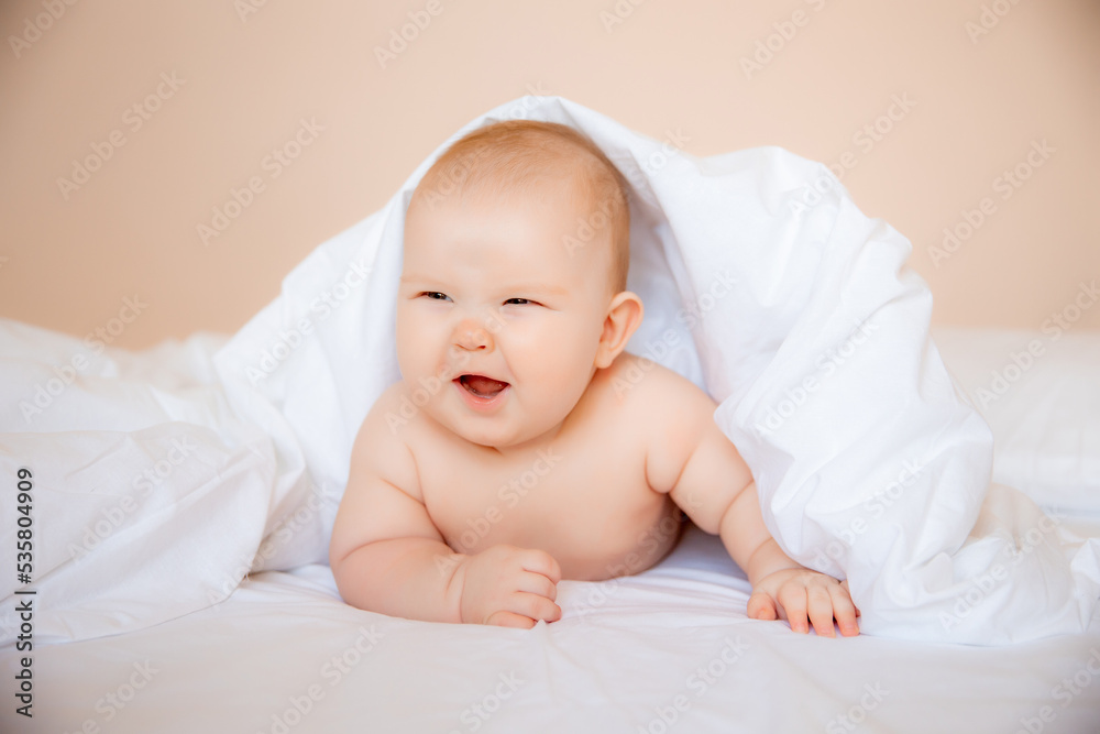 baby boy in a diaper is lying on a white sheet, covered with a blanket in the bedroom on the bed