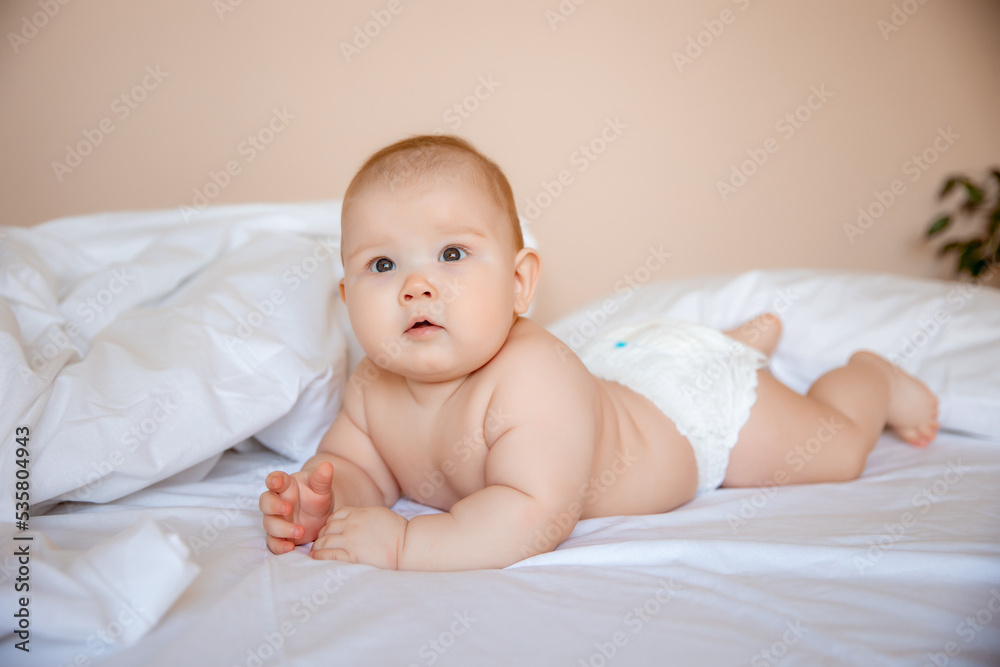 cute baby boy in a diaper is lying on a white sheet, covered with a blanket in the bedroom on the bed cute baby boy in a diaper is lying on a white sheet, covered with a blanket in the bedroom on the bed