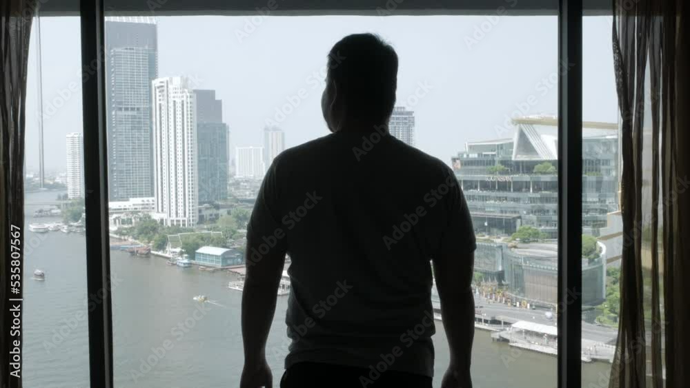 asian man opens the curtain of big window with view of icon siam department store on the riverside