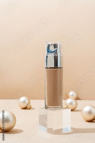 A minimalistic scene of foundation bottle on glass podium with christmas decorative balls on beige background