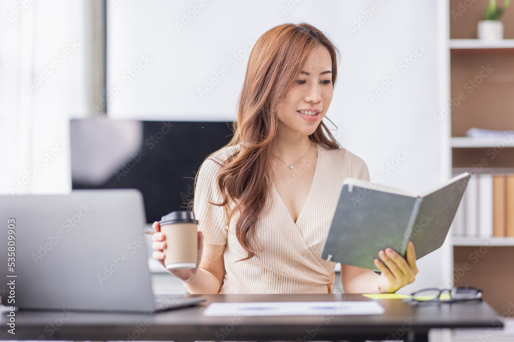 Asian Businesswoman holding notes and working on a laptop computer in the workplace, doing document planning analyzing the financial report, business plan investment, finance analysis concept. Asian Businesswoman holding notes and working on a laptop computer in the workplace, doing document planning analyzing the financial report, business plan investment, finance analysis concept.