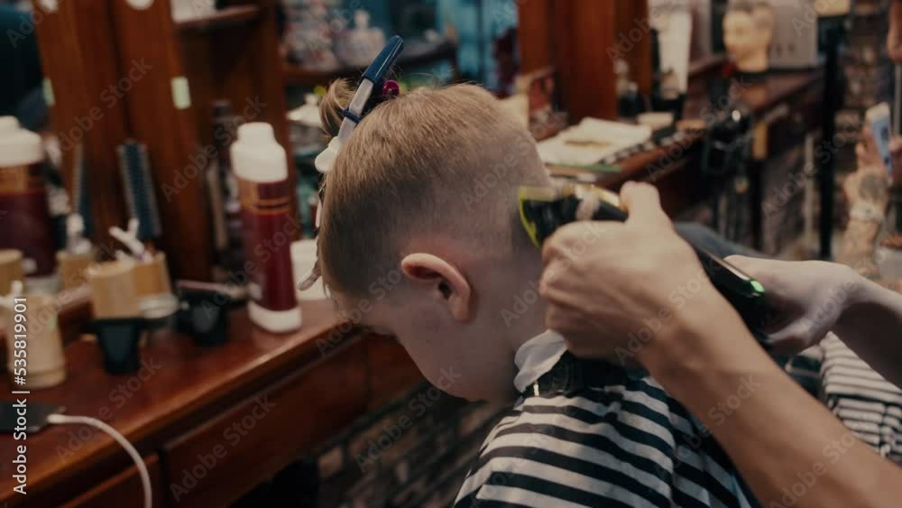 Fashionable hairdresser cuts a child's hair with a clipper in a barbershop. Close up side view portrait Men's hairstyle and haircut in the salon. Fashionable hairdresser cuts a child's hair with a clipper in a barbershop. Close up side view portrait Men's hairstyle and haircut in the salon.