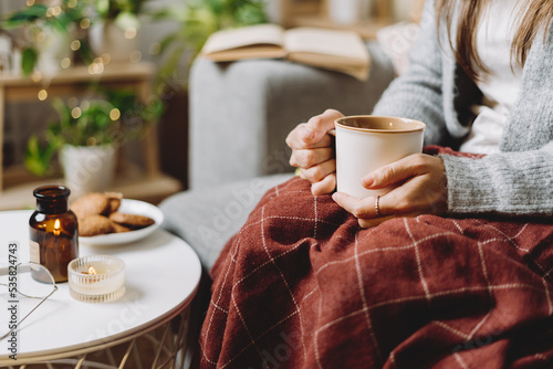 Papier peint Cozy woman legs in knitted winter warm sweater and checkered plaid drinking hot cocoa or coffee in mug, sitting on couch at home