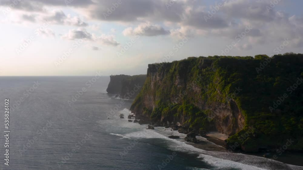 Silhouette of majestic Uluwatu cliffs standing tall beside coastline of beach and low tides moving towards them. Silhouette of majestic Uluwatu cliffs standing tall beside coastline of beach and low tides moving towards them.