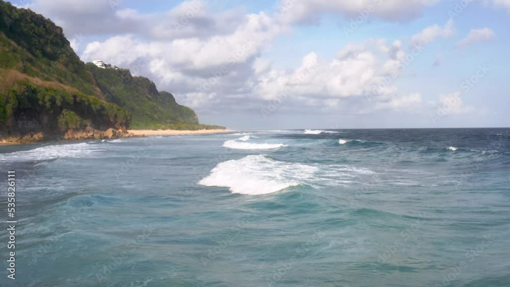 Calm and low tides moving towards the shore with huge cliffs on bright sunny day. Low angle view. Calm and low tides moving towards the shore with huge cliffs on bright sunny day. Low angle view.