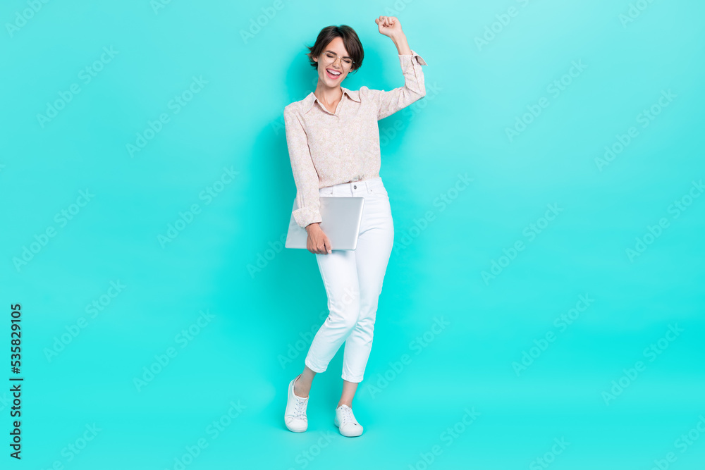 Full length photo of satisfied lady hand arm hold netbook rejoice pass online exam fist yes empty space isolated on cyan color background