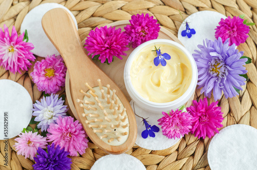 Yellow hair mask (banana face cream, shea butter mask, mango body butter) in a small white jar and wooden hair brush. Natural skin and hair care treatment concept. Top view, copy space.