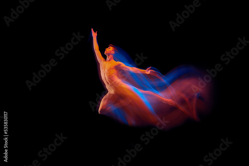 Young graceful and flexible shirtless male ballet dancer dancing isolated on dark background in glowing colorful neon light. Grace, art, beauty