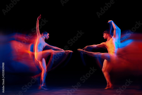 Confrontation between two. Couple of graceful and fragile ballet dancers in action isolated over black background in mixed neon light. Futurism, fantasy, miracle.