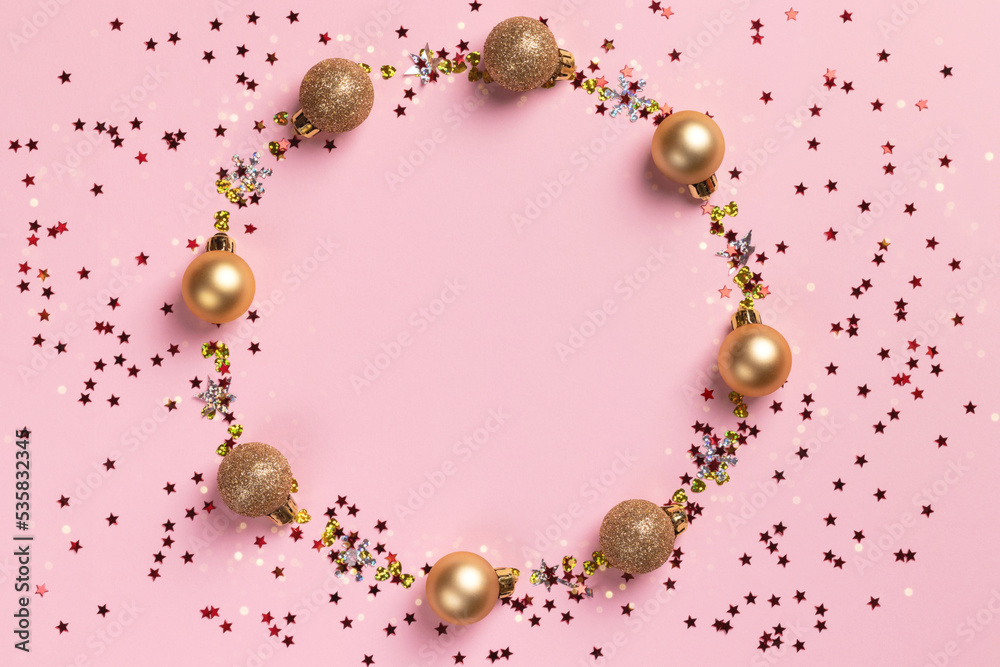 Circle frame of golden Christmas balls and glitter confetti stars on pink background Circle frame of golden Christmas balls and glitter confetti stars on pink background