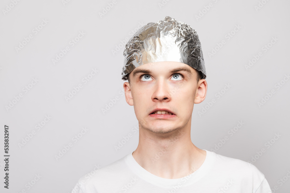 Paranoid young man wearing tin foil hat studio shot on gray background Paranoid young man wearing tin foil hat studio shot on gray background