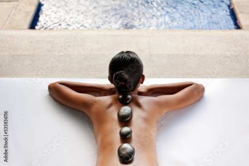 Woman receiving Hot Stone Massage in the gazebo of a private pool villa at a spa resort. Bali, Indonesia