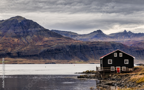 Old wooden boathouse, fjords and mountains in Djupivogur, Eastfjords, Iceland. Picturesque view of calm waters under a stormy sky. Autumn colours are picked out on the mountainside photo