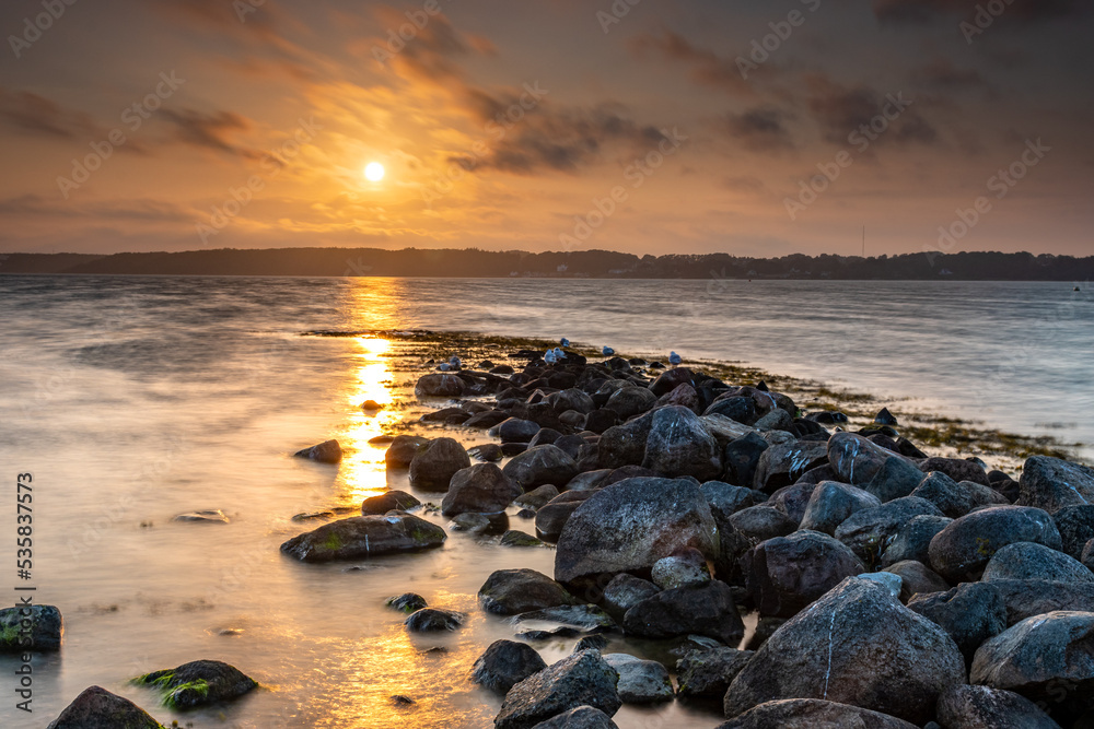 Mole made of stones leading to the Flensburg Fjord, Germany, Baltic Sea. Backlit sunset