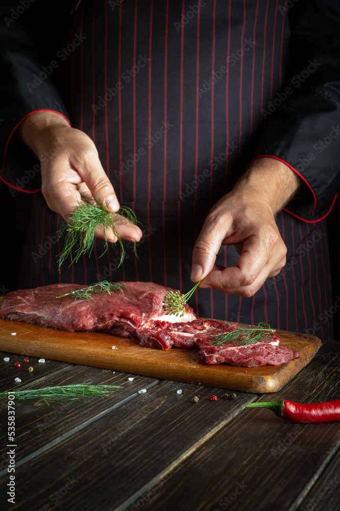 The chef putting dill leaves on meat before grilling. Space for recipe or hotel menu on dark background