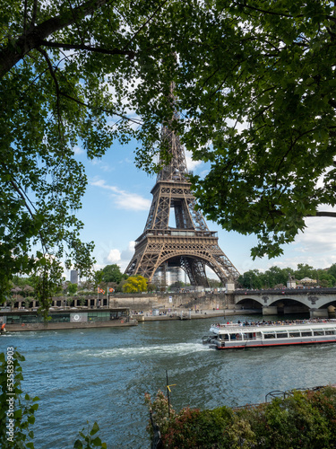Eiffel tower across Seine River through trees as boat passes
