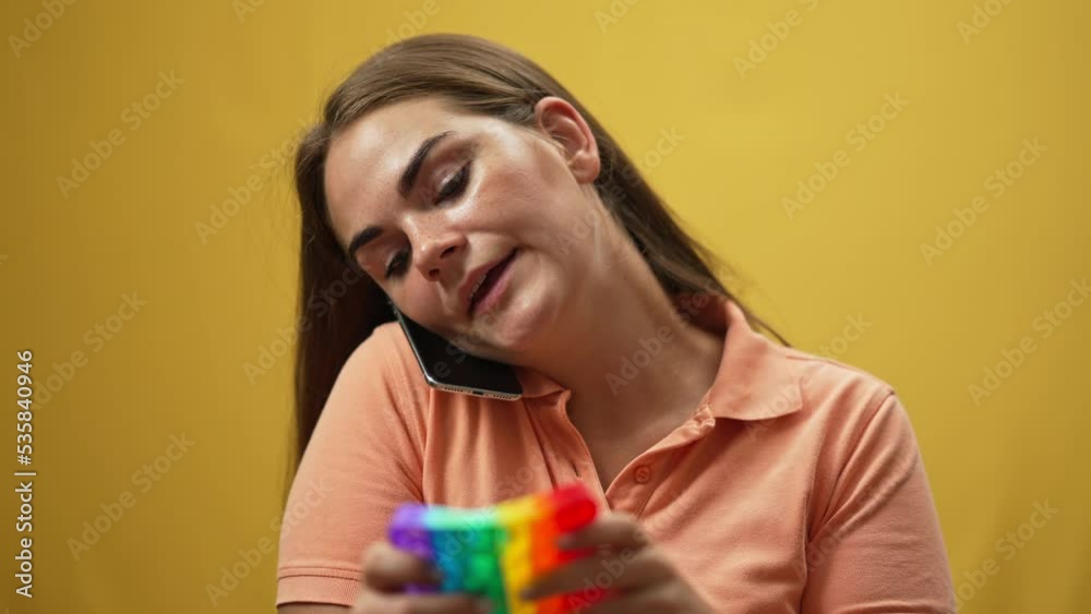 Portrait of confident woman playing fidget toy talking on phone holding smartphone with shoulder. Brunette charming Caucasian lady chatting calming down with sensory toy in slow motion at background Portrait of confident woman playing fidget toy talking on phone holding smartphone with shoulder. Brunette charming Caucasian lady chatting calming down with sensory toy in slow motion at background