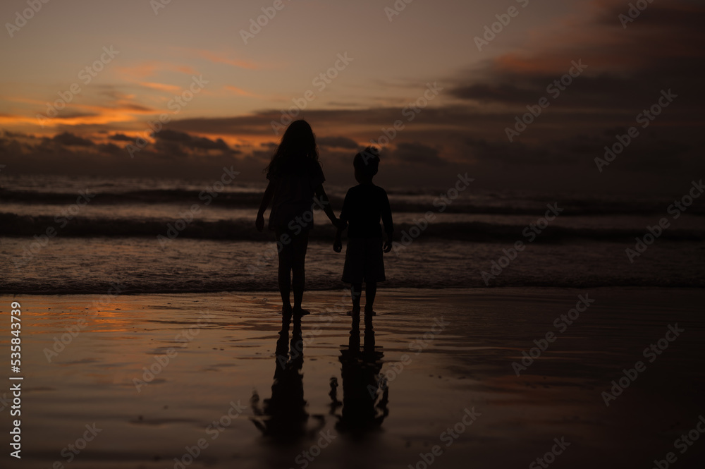 Silhouette portrait of lovely sibling on the beach shore at sunset having fun time.