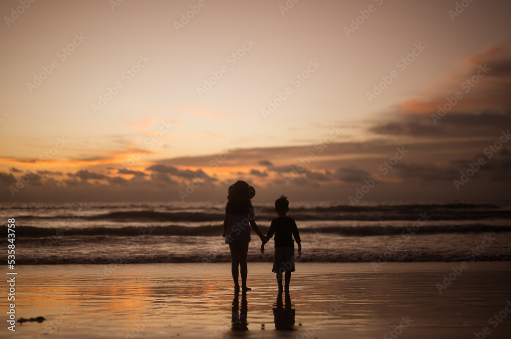 Silhouette portrait of lovely sibling on the beach shore at sunset having fun time.