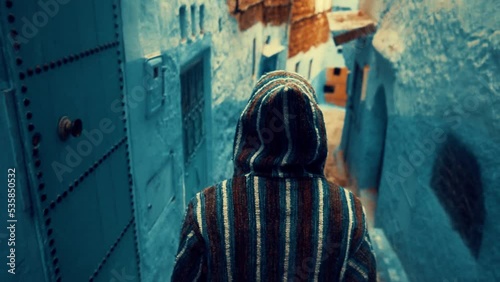 A man walking through a blue and white street in Old Medina of Chefchaouen city, Morocco.