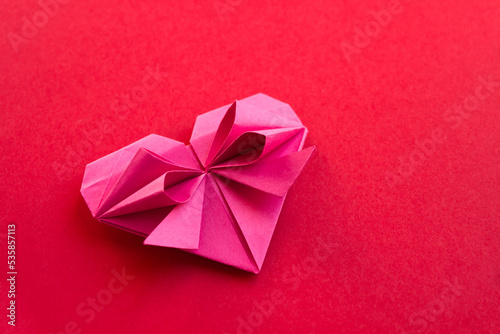 Pink paper heart origami isolated on a red background