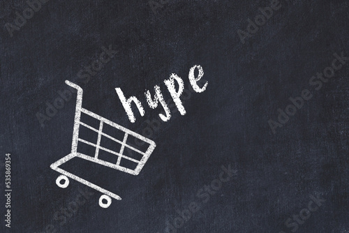 Chalk drawing of shopping cart and word hype on black chalboard. Concept of globalization and mass consuming
