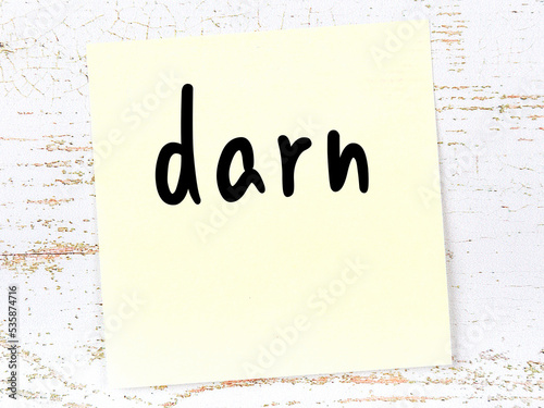 Yellow sticky note on wooden wall with handwritten word darn