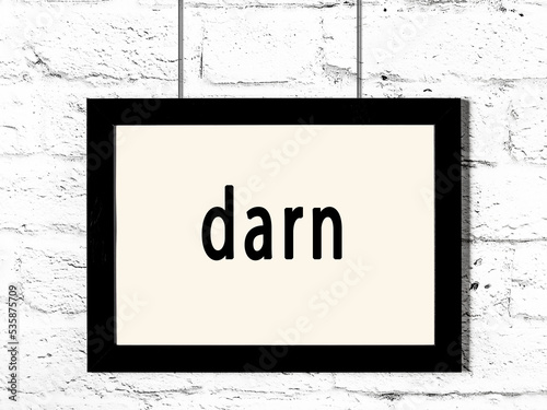 Black frame hanging on white brick wall with inscription darn