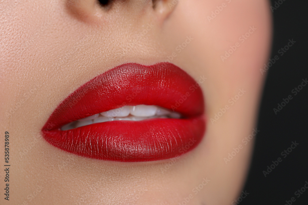 Young woman wearing beautiful red lipstick on black background, closeup Young woman wearing beautiful red lipstick on black background, closeup