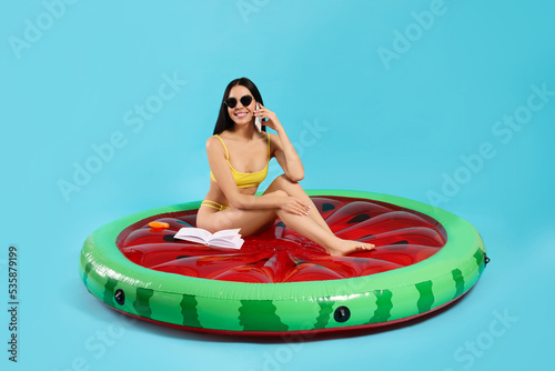 Young woman in stylish sunglasses on inflatable mattress against light blue background