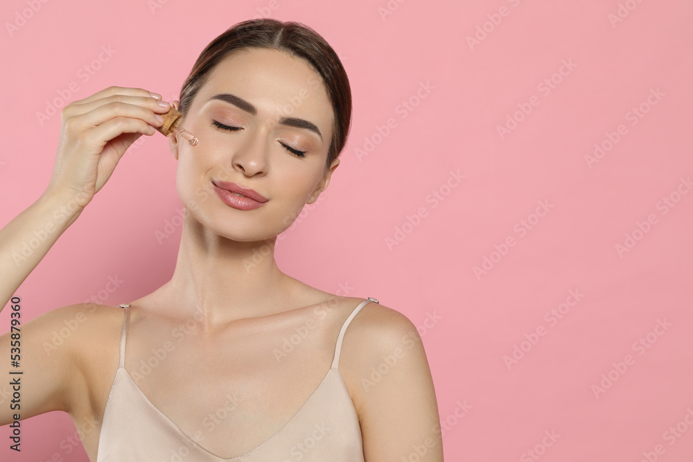Young woman applying essential oil onto face on pink background, space for text Young woman applying essential oil onto face on pink background, space for text