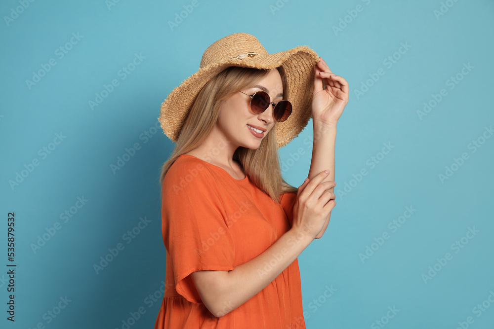 Beautiful young woman wearing straw hat and sunglasses on light blue background. Stylish headdress Beautiful young woman wearing straw hat and sunglasses on light blue background. Stylish headdress