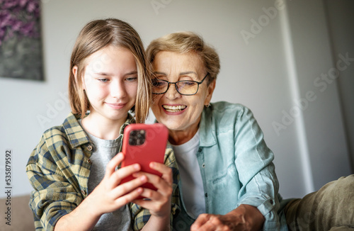 Obraz na płótnie Smiling girl granddaughter with happy grandmother having fun and using looking at smartphone screen w salonie