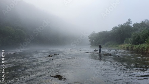 Silhouette of a fisherman, a rod and a breathtaking scene in Bieszczady mountains with fog on San river. Article about fishing day hunting for a trout.