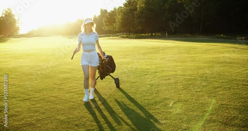Young female golfer with a club walks on the golf course. beautiful sunlight. High quality 4k footage