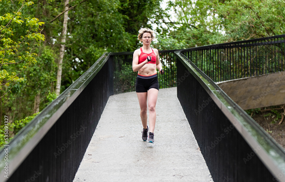 Healthy thirty year old woman running on a pedestrian bridge outdoors