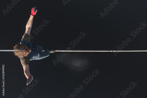 A male tightrope walker walks a slackline stretched over the mirror surface of the water. Drone view. photo