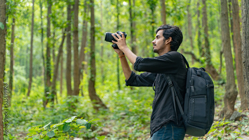 Canvas Print Young photographer standing in the nature, taking picture with professional came